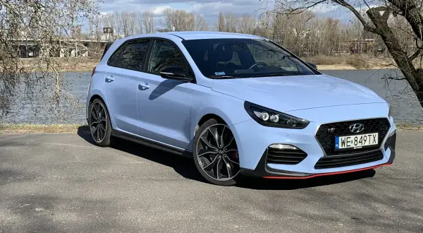Niebieski Hyundai i30 N z czerwonymi akcentami stoi nad jeziorem, gotowy na wiosenną przejażdżkę.