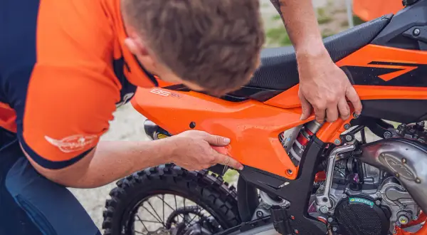 Mecánico ajusta panel en KTM 300 TPI. Se aprecia el motor y la rueda trasera.