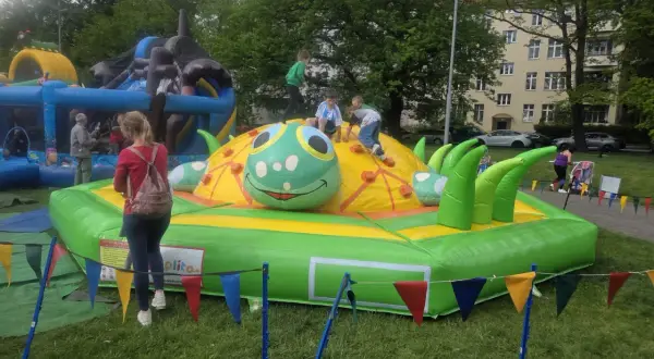 Dzieci bawią się na dmuchanej gąsienicy, która jest jedną z atrakcji dla 3 latka. W tle widać inne dmuchańce i budynek mieszkalny.