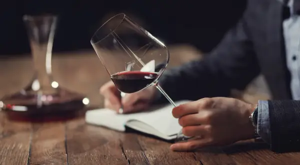 Un homme déguste un verre de vin rouge, notant ses impressions pour la saint-emilion grand cru classé liste.