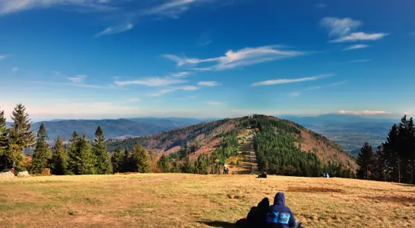 Widok na góry w Bielsku-Białej. Dwie osoby siedzą na trawie, podziwiając jesienny krajobraz i panoramę Beskidów.