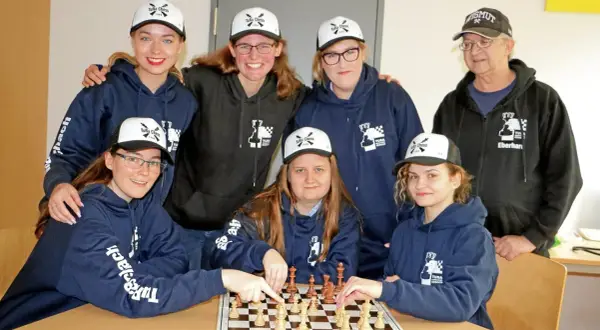 Grupa osób w bluzach i czapkach z logo "TuRa Chess" gra w szachy.