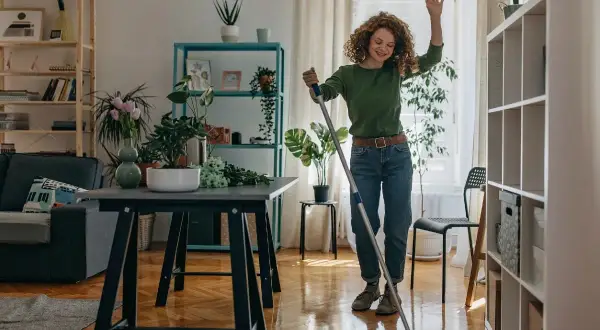Donna sorridente lava il pavimento con uno straccio, un esempio di come tenere in ordine la casa con gioia.