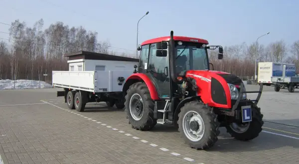 Czerwony traktor z przyczepą, gotowy do egzaminu na prawo jazdy na traktor. Litera "L" na zderzaku.