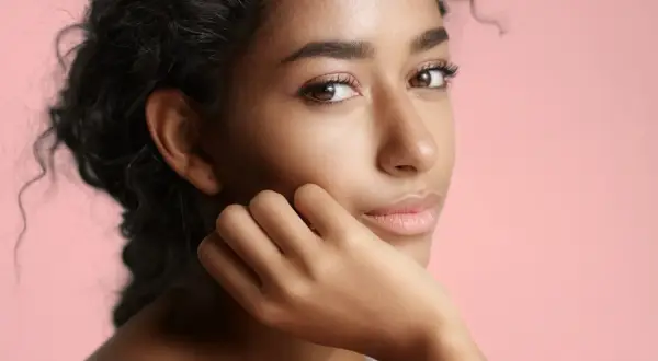 Portrait d'une jeune femme à la peau de couleur de peau olive, aux cheveux sombres et bouclés, posant sa main sur sa joue.