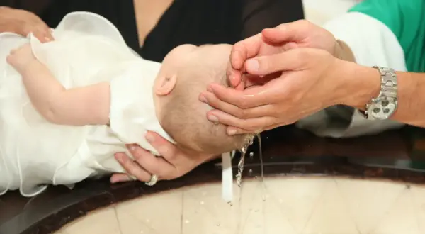 Chrzest dziecka: ręce księdza polewają głowę niemowlęcia wodą.