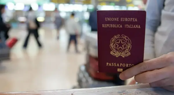 Włoski paszport w dłoni, gotowy do podróży. W tle lotniskowy gwar, idealny na wakacje bez paszportu.