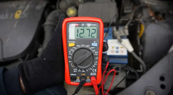 Multimetr pokazuje 12.72V, co jest kluczowe, jak sprawdzić akumulator. Pomiar napięcia baterii w samochodzie.