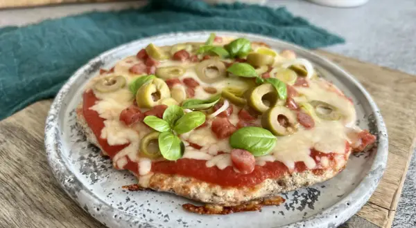 Mini pizza z serka wiejskiego, z sosem pomidorowym, oliwkami, kiełbaską i bazylią, na talerzu.