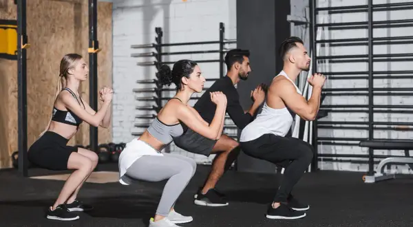 Uomini e donne eseguono squat a corpo libero in palestra, concentrati sull'esercizio.