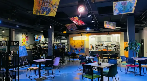 Wnętrze Oria Magic House z kolorowymi obrazami na suficie i ścianach. Stoliki i krzesła tworzą przytulną atmosferę, idealną do przeglądania menu.