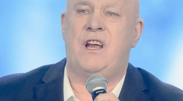 Ryszard Rynkowski śpiewa do mikrofonu, ubrany w marynarkę i białą koszulę.