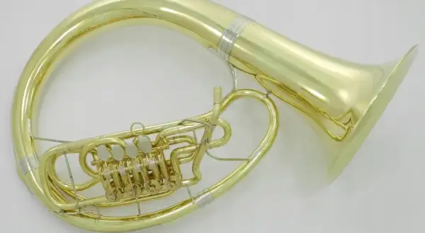 Błyszczący, złoty, duży instrument dęty z zaworami, owinięty wokół ciała muzyka, gotowy do wydobycia głębokich dźwięków.