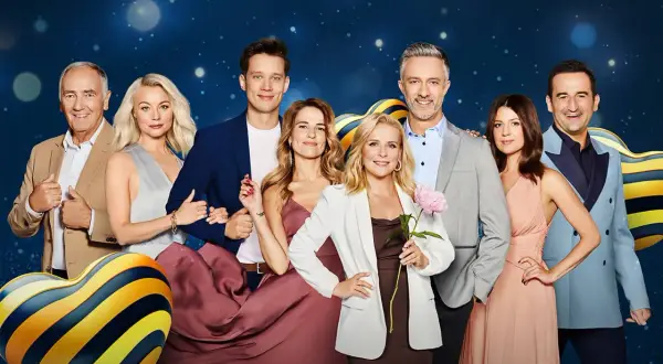 Grupa uśmiechniętych osób, w tym 19+ obsada, pozuje na tle niebieskiego, błyszczącego tła.