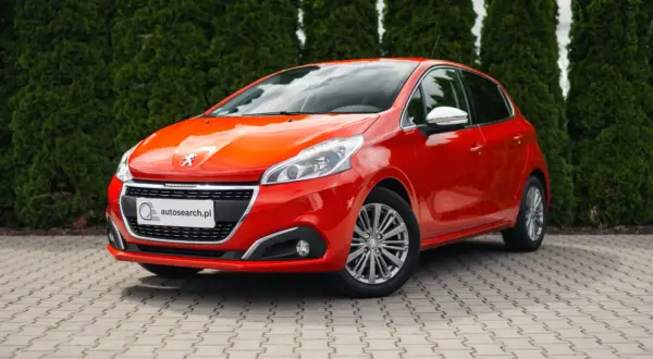 Czerwony Peugeot 208 z błyszczącymi światłami, idealny na egzamin na prawo jazdy.