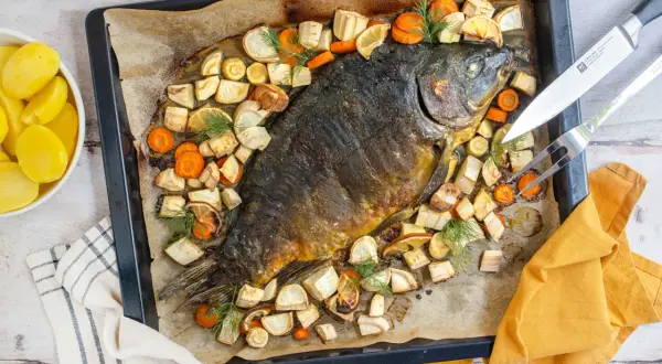 Schuppenkarpfen zubereiten: Ganzer Fisch mit Wurzelgemüse und Zitrone auf einem Blech gebacken. Daneben gekochte Kartoffeln.