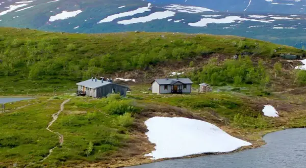 Fjällstugor vid en sjö, med snöfläckar kvar på sluttningarna. En idyllisk vy från Saltoluokta mot Kvikkjokk.