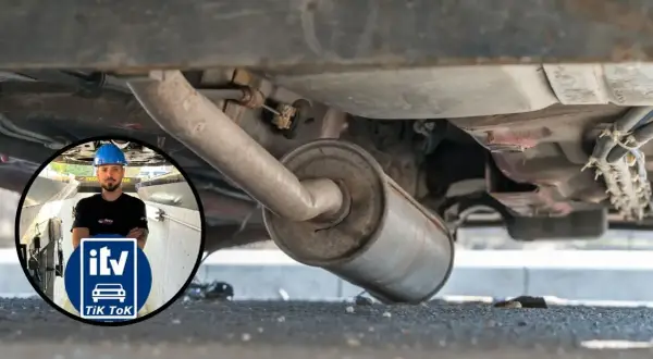 Inspección del tubo de escape de un coche. Un mecánico con casco azul supervisa la revisión.