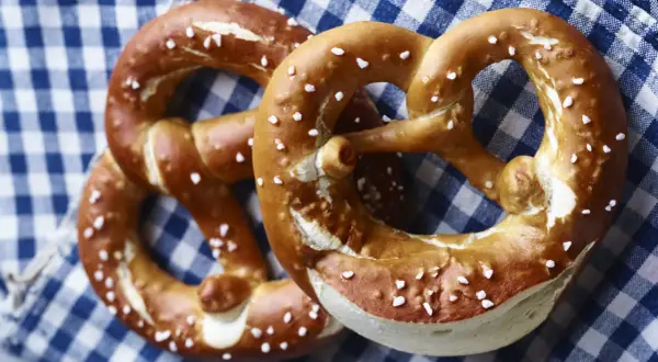 Zwei goldbraune Brezen mit grobem Salz liegen auf kariertem Stoff.