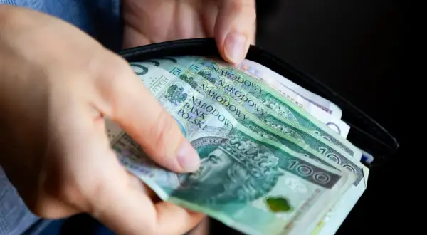 Ręce wkładają do portfela polskie banknoty. Czy można wypłacić pieniądze z OFE?