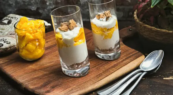 Zwei Gläser mit Mango-Creme und Kekskrümeln, daneben ein Glas mit Mangostücken. Perfekt für leichte ricotta rezepte.