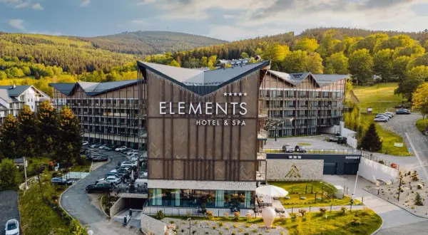 Nowoczesny hotel Elements Hotel & Spa w otoczeniu górskiego lasu, z widocznym logo hotelu.
