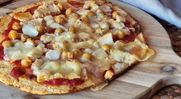 Pizza sin queso con garbanzos y trozos de queso derretido sobre una base crujiente.