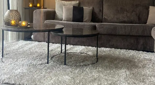 Gemütliches Wohnzimmer mit einem Sofa in greige Farbe, zwei Marmor-Couchtischen und einem flauschigen Teppich.