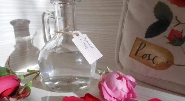 Szklana butelka z etykietą "Hydrolat z róży" i płatkami róż. Idealny sposób, jak zrobić hydrolat w domu.