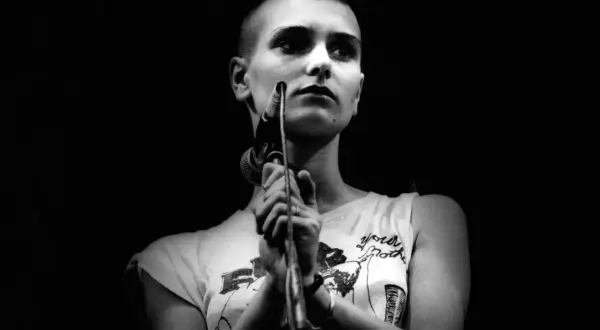 Sinéad O'Connor śpiewa "Nothing Compares 2 U", jej twarz jest oświetlona, a ona trzyma mikrofon.