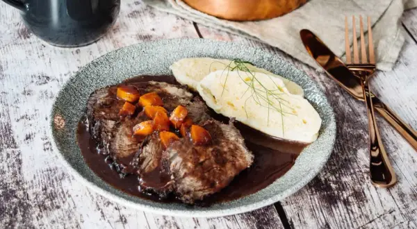 Klassisches Sauerbraten Rezept im Backofen: Zartes Rindfleisch in dunkler Soße mit Karotten und Klößen, garniert mit Dill.