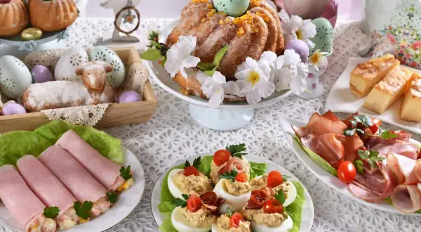 Udekorowany stół na śniadanie wielkanocne: babka, baranek, jajka faszerowane, wędliny i ciasto.