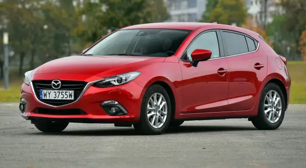 Czerwona Mazda 3 2015 na parkingu, z widocznym numerem rejestracyjnym WY 3755W.