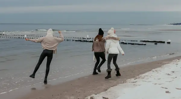 Trzy dziewczyny cieszą się zimą nad morzem, biegając po plaży z resztkami śniegu.