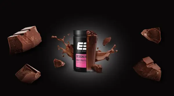 Schokoladenstückchen umgeben einen Becher Designer Whey Protein. Die Frage, ob Proteinpulver krebserregend ist, bleibt unbeantwortet.