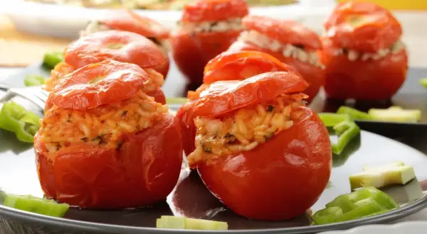 Pomodori ripieni di riso, un piatto gustoso e colorato, serviti su un piatto scuro con peperoni verdi.