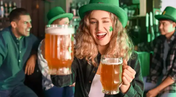 Ragazza con cappello verde e trucco trifoglio offre due boccali di birra irlandese rossa in un pub festoso.