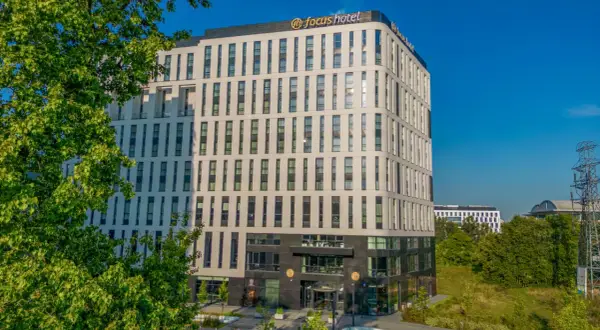 Nowoczesny budynek Focus Hotel Premium Warszawa z zielenią i błękitnym niebem. Idealne miejsce na pobyt.