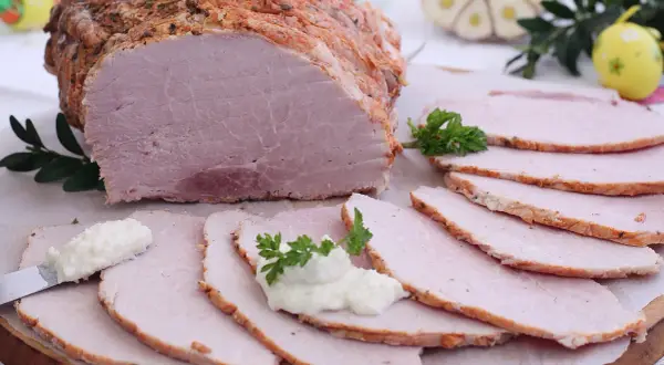 Soczysta szynka pieczona w rękawie, pokrojona w plastry, z chrzanem i natką pietruszki. Idealna na wielkanocny stół.
