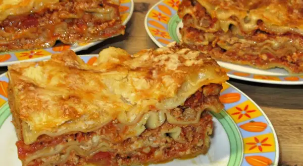 Prosty przepis na lasagne z mięsem mielonym. Pyszne, warstwowe danie z makaronem, sosem mięsnym i serem, podane na kolorowych talerzach.