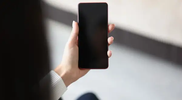 Dłoń trzyma telefon z czarnym ekranem, być może z powodu pogorszenia jakości zdjęć w telefonie.
