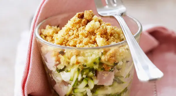 Un délicieux crumble de courgettes, jambon et fromage, servi dans un verre, prêt à être dégusté avec une fourchette.