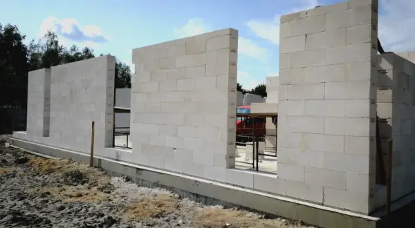 Budowa domu z bloczków z betonu komórkowego. Ściany wznoszą się nad fundamentem, tworząc zarys pomieszczeń.