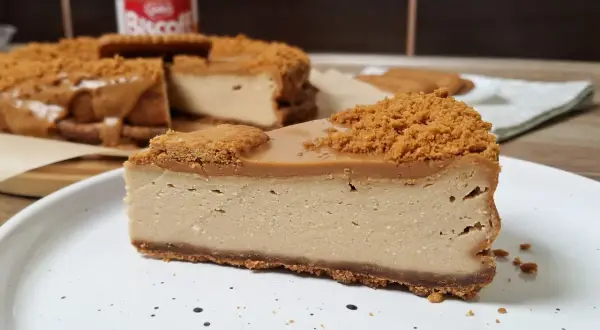 Kawałek pysznego sernika Lotus na talerzu, z widocznym słoiczkiem kremu Lotus w tle.