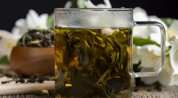 Aromatyczna herbata jaśminowa w szklance, z kwiatami jaśminu w tle. Poznaj jaśmin właściwości.
