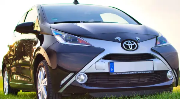 Czarny Toyota Aygo, jeden z popularnych japońskich marek aut, na tle zielonej trawy.