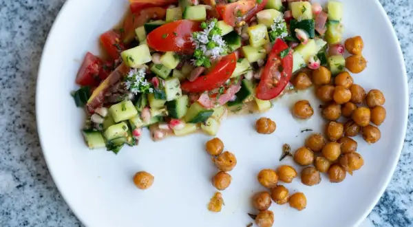 Salade colorée de tomates, concombres et pois chiches rôtis, garnie de petites fleurs blanches.