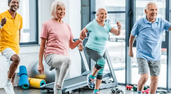 Quatre seniors souriants font de l'exercice ensemble. Voici 5 arguments pour le sport : vitalité, joie, santé, longévité et bien-être.