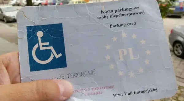 Karta parkingowa dla niepełnosprawnych z symbolem wózka inwalidzkiego i oznaczeniem PL. Dokument uprawnia do parkowania w całej Unii Europejskiej.