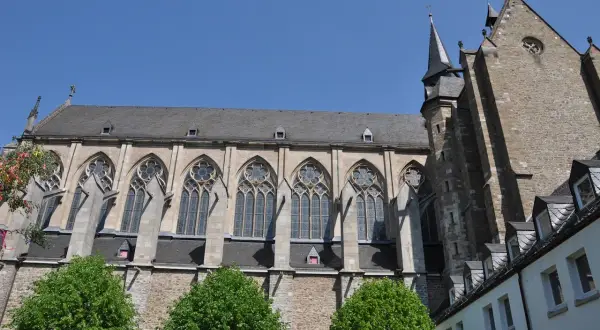Der Altenberger Dom ragt mit seinen gotischen Fenstern und steinernen Mauern in den blauen Himmel. Grüne Bäume säumen das imposante Bauwerk.